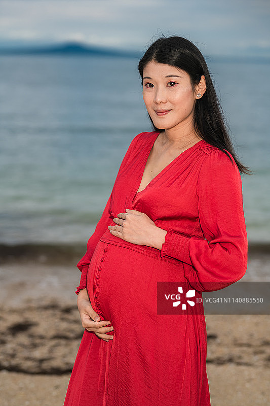 一位身穿红色连衣裙的孕妇躺在美丽的沙滩上图片素材