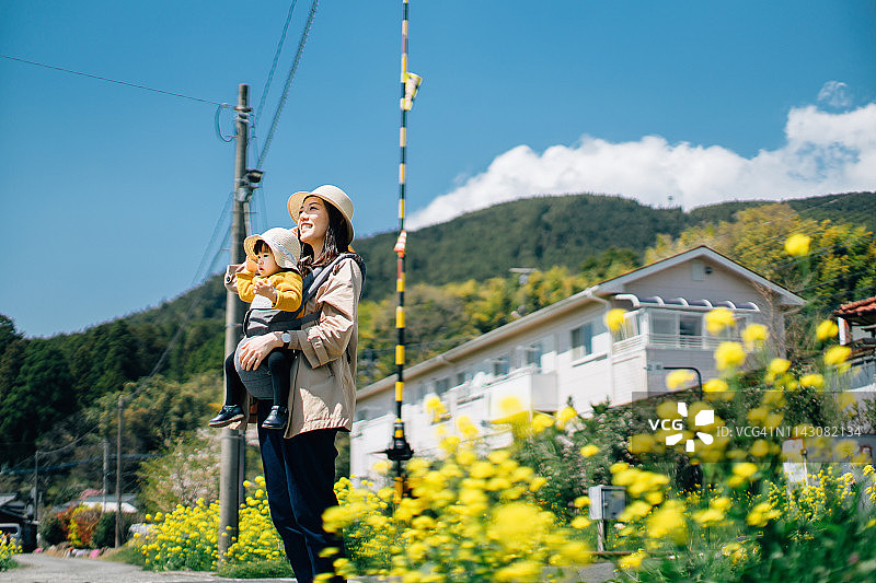 快乐的母亲和女儿在大自然中旅行，在油菜地上，在蓝天下散步图片素材