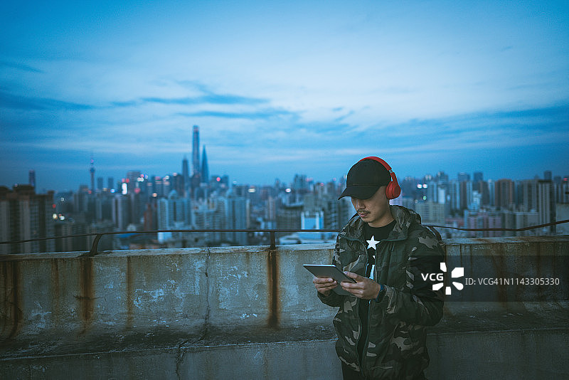 在中国上海的一幢高楼的屋顶上，一名男子戴着耳机使用平板电脑图片素材