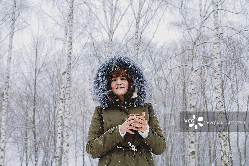 低角度的女人拿着茶，而站在公园里的树在冬天图片素材