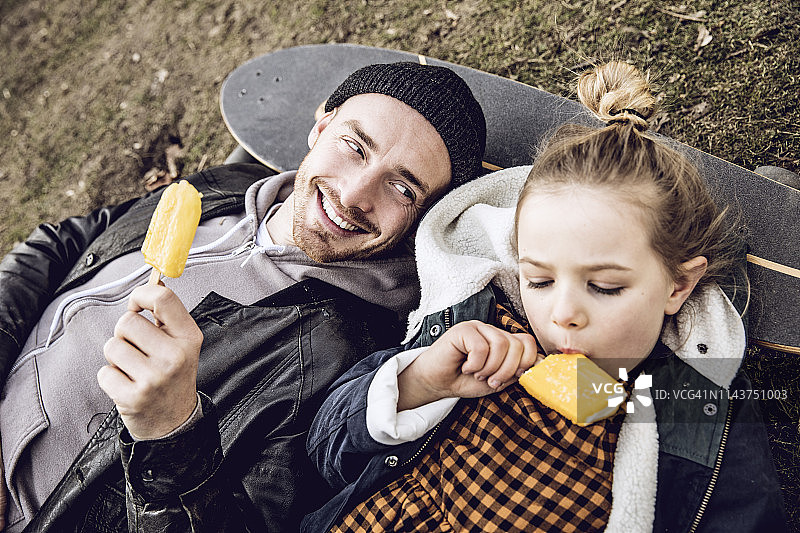 父亲和女儿在滑板上休息，吃着冰淇淋图片素材