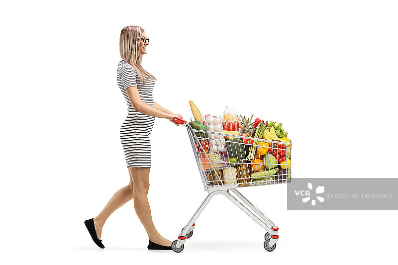 年轻的金发女人推着一个装着食品的购物车走着图片素材