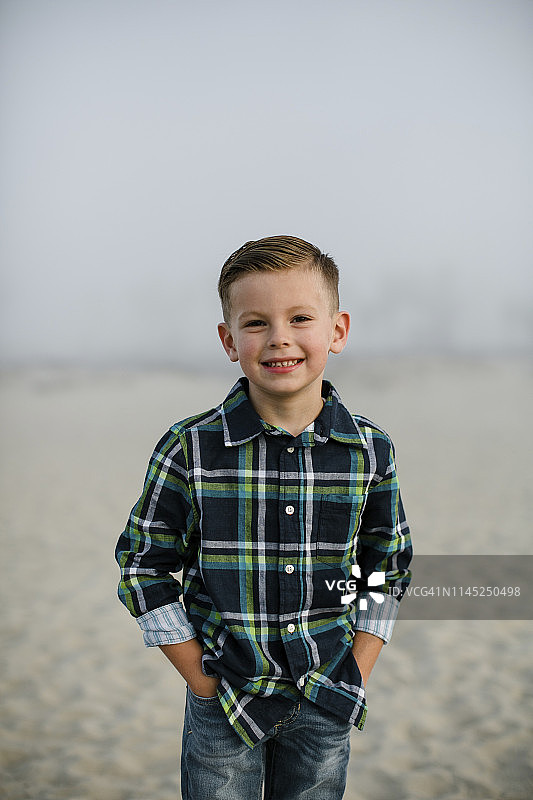 在雾霾天气里，可爱的男孩双手插在口袋里站在海滩上图片素材