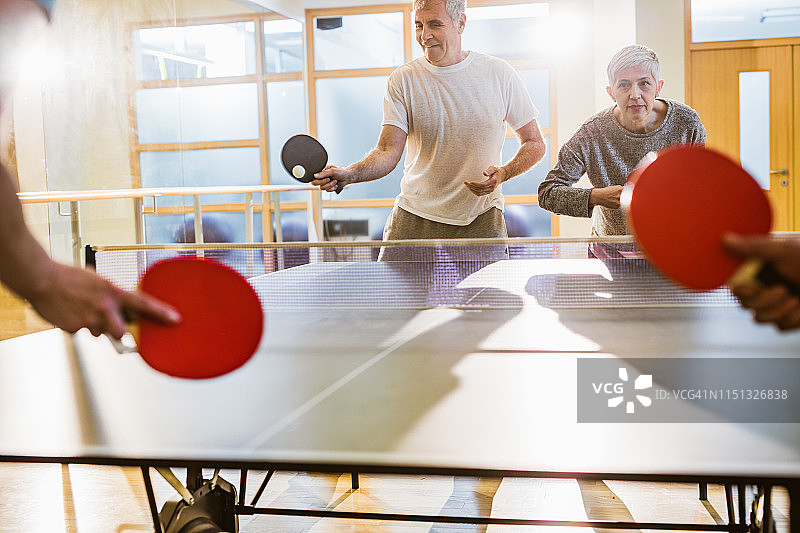 一群活跃的老年人在一家健身俱乐部打乒乓球。图片素材