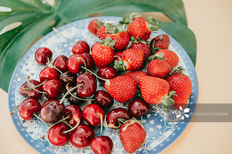 盘子里的红色水果。蓝色陶瓷盘子里的草莓和樱桃图片素材
