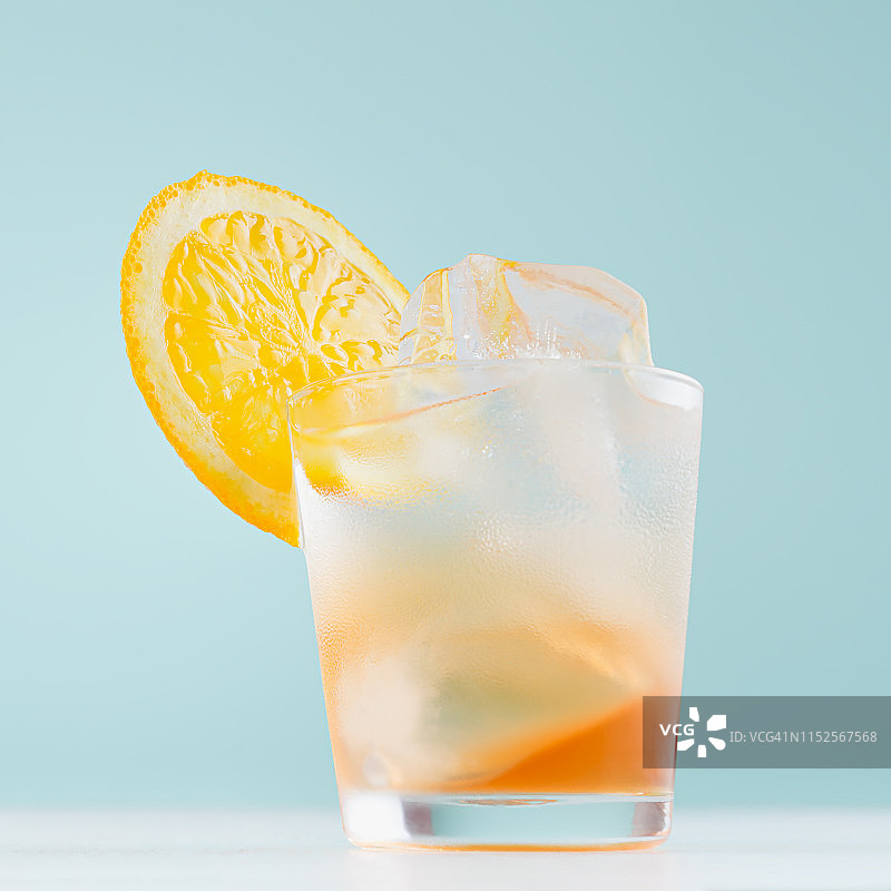 热带清爽的水果饮料与桔子片，冰在白色木板雾蒙蒙的小酒杯，柔和的绿色内部，正方形。图片素材