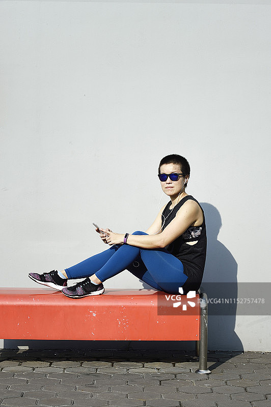一个女人在健身后坐在橙色的长椅上看手机图片素材
