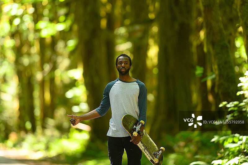 带着滑板的男人在森林里搭便车图片素材
