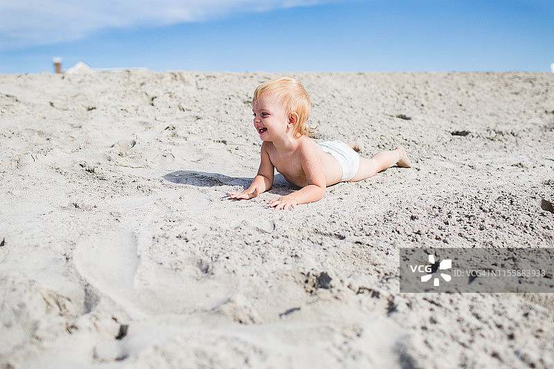 金发白种小孩在沙丘上微笑在她的尿布图片素材