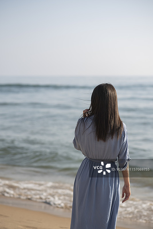 一个年轻女子站在海滩上的后视图图片素材