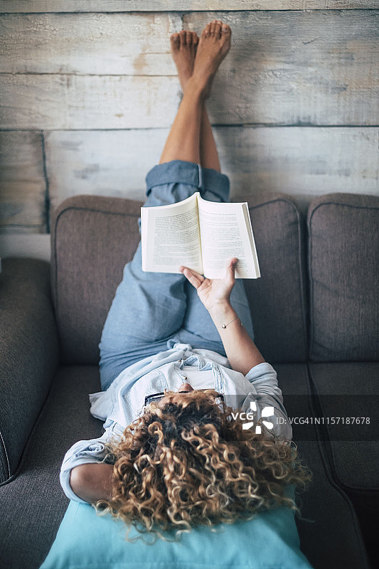 一个女人躺在家里的沙发上看书图片素材
