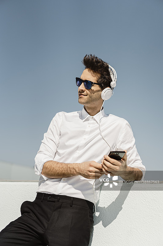 商人在屋顶平台上用耳机和智能手机听音乐的肖像图片素材