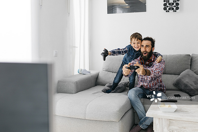 兴奋的爸爸和儿子在家里玩电脑游戏图片素材