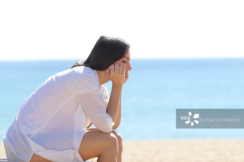 一个焦虑的女人坐在海滩上的侧面图片素材