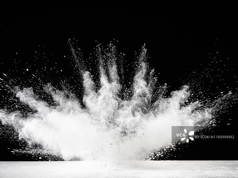 在黑色的背景上，一团白色的烟雾和粉末颗粒的撞击造成的爆炸。图片素材