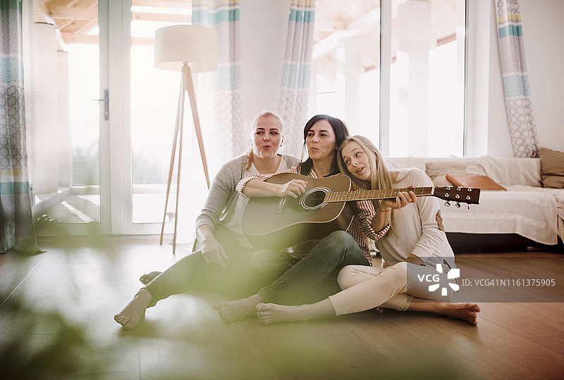 一个有两个女儿的成熟女人坐在家里的地板上弹吉他图片素材