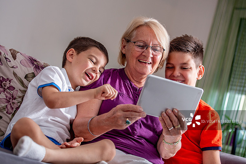 奶奶和孙子正在用平板电脑通过互联网打电话与爷爷在线交谈图片素材