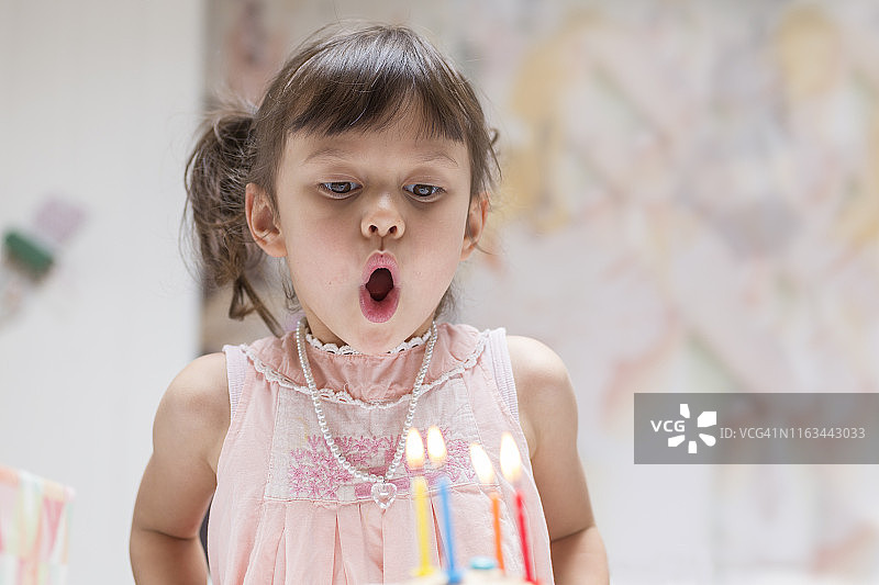 小女孩吹灭生日蛋糕上燃烧的蜡烛的肖像图片素材