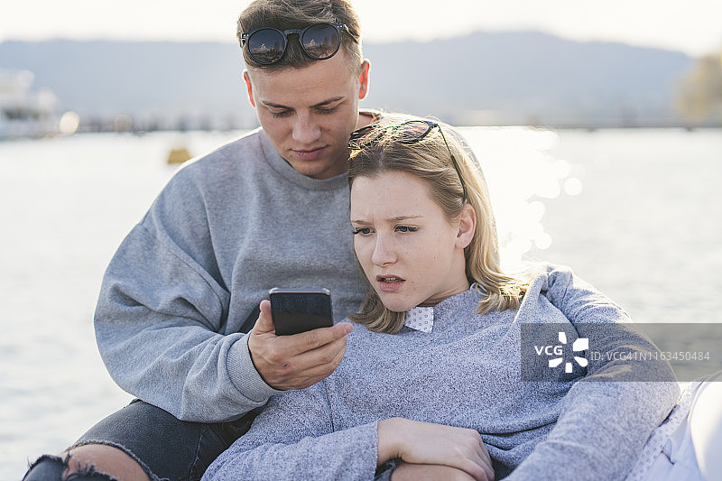 年轻夫妇在苏黎世湖码头上看手机，瑞士苏黎世图片素材