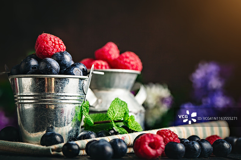 深色背景上的杯子里的覆盆子和蓝莓。夏日与健康的饮食理念。背景与复制空间。有选择性的重点。水平的。图片素材