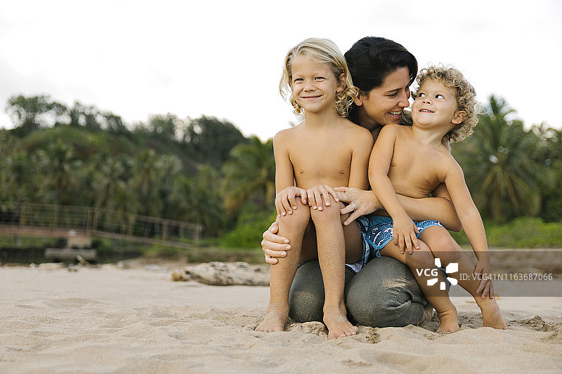一个女人和她的儿子坐在沙滩上她的腿上图片素材