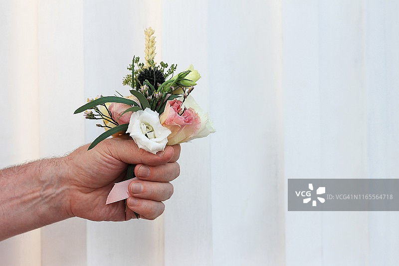 一个男人的手拿着一小束美丽的花在一个灯光背景。花要送，拷贝空间。图片素材