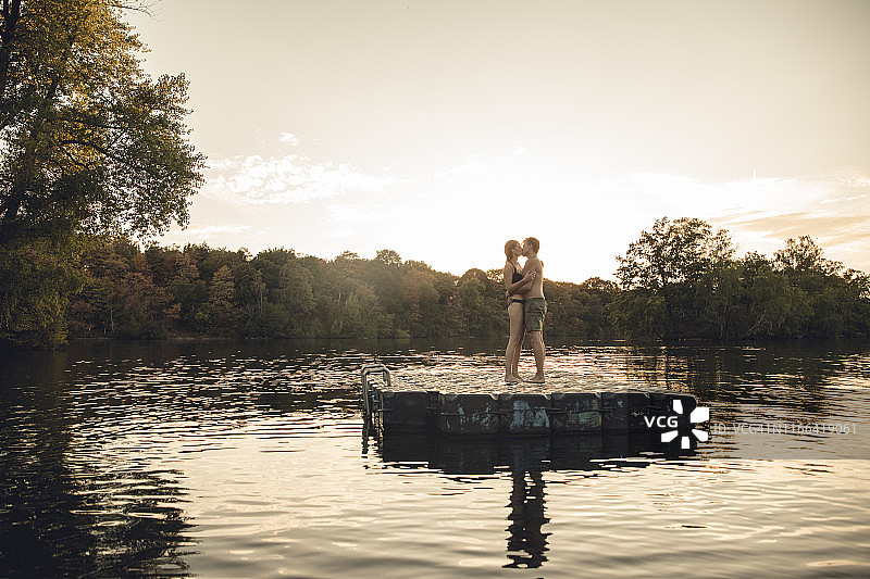 一对年轻的情侣站在湖边的沐浴平台上，拥抱亲吻图片素材