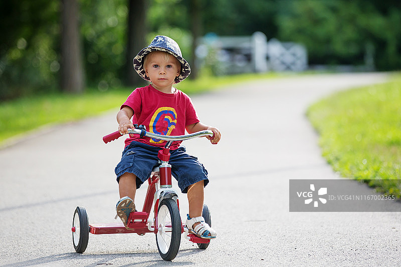 可爱的蹒跚学步的小男孩，在公园里骑三轮车，夏日时光图片素材
