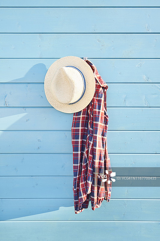 草帽和红格子衬衫挂在蓝色的木墙上图片素材