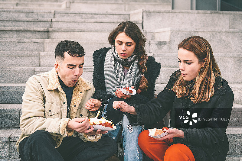 三个年轻的旅行者在柏林户外吃咖喱香肠图片素材
