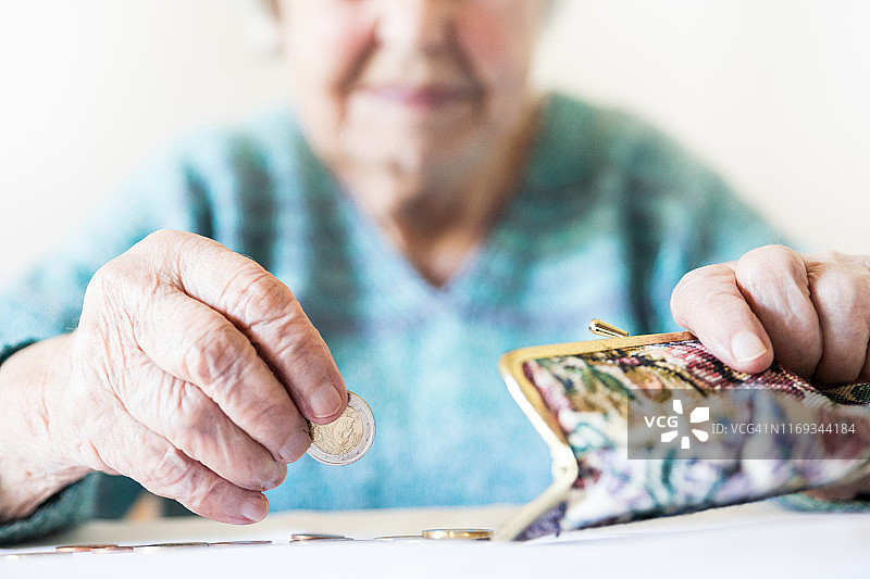 详细的特写照片，不认识的老年妇女的手数剩余的硬币，从养老金在她的钱包付款后。图片素材