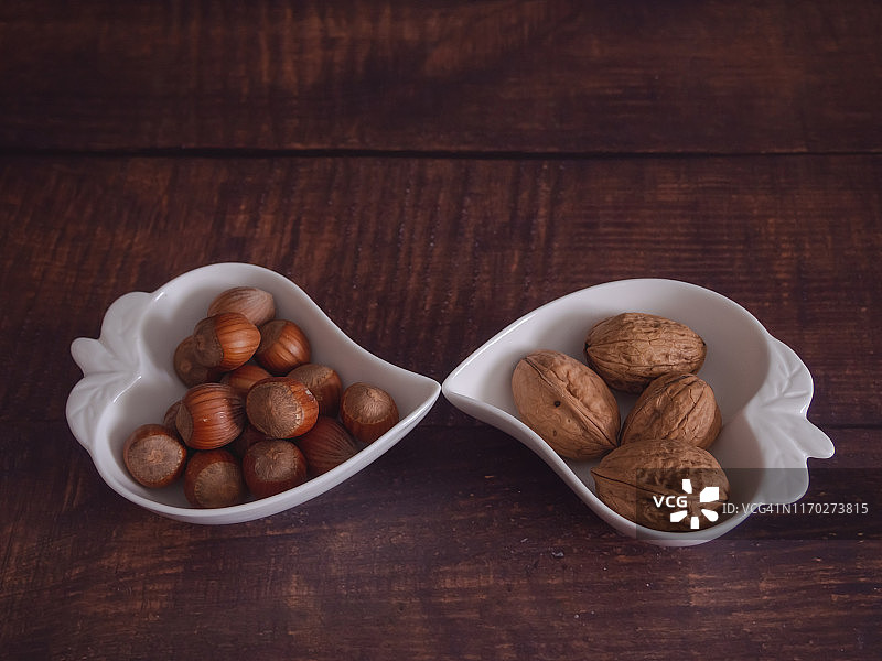 秋果:两组核桃和榛子，放在一个旧木桌上的心形瓷碗里图片素材