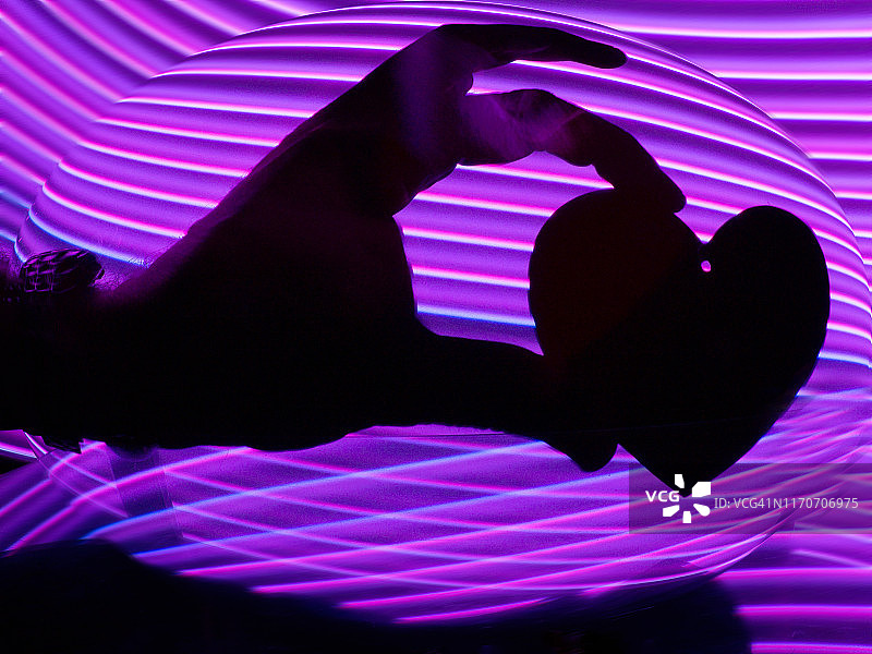 在一个紫色的虚拟环境中，人类的手握着一颗心。图片素材