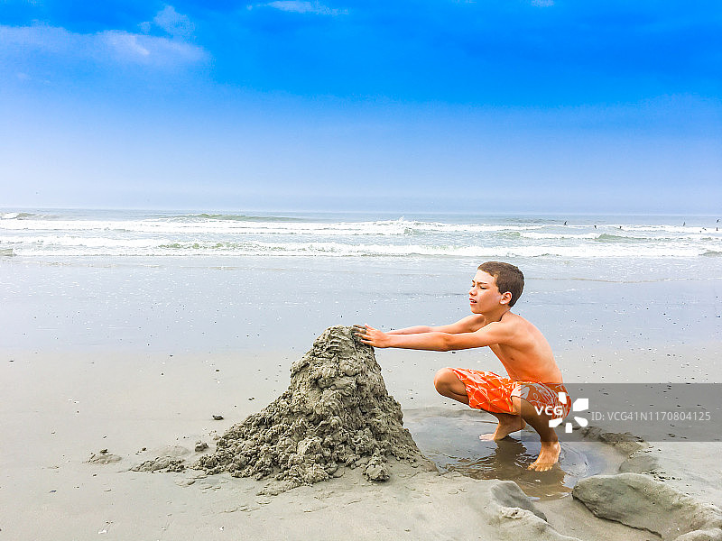 男孩在沙滩上挖沙子图片素材