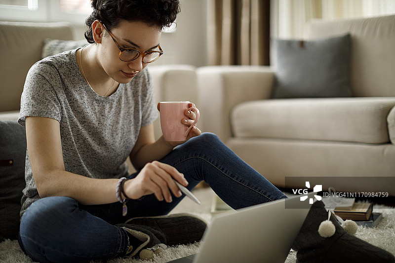 年轻女子在家里用笔记本电脑喝咖啡图片素材