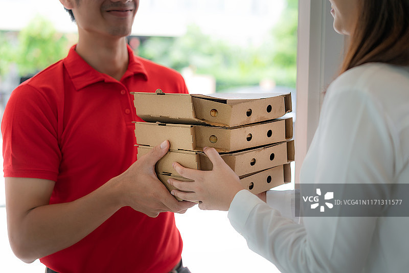 亚洲男人用纸盒送披萨给亚洲女性顾客。图片素材