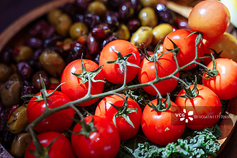 木盘上放着成熟的西红柿、橄榄和绿叶蔬菜图片素材