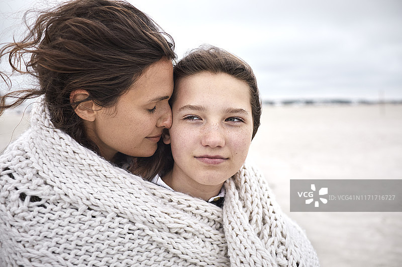 沙滩上，一个年轻的女人和一个女孩裹着毯子图片素材