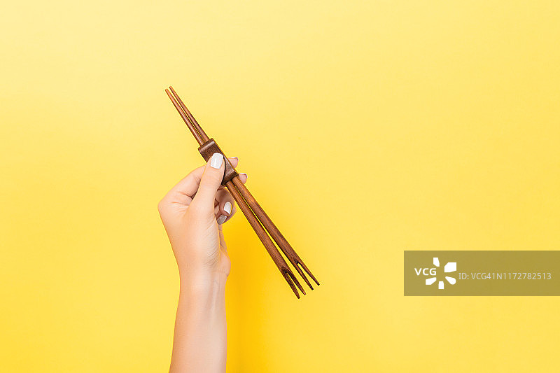 黄色背景上的女性手拿筷子。寿司概念与空空间为您的想法图片素材
