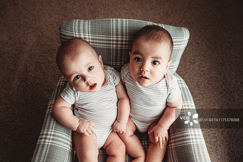 7个月大的男性异卵双胞胎坐在格子摇椅上，穿着一件灰色和白色连体衣图片素材