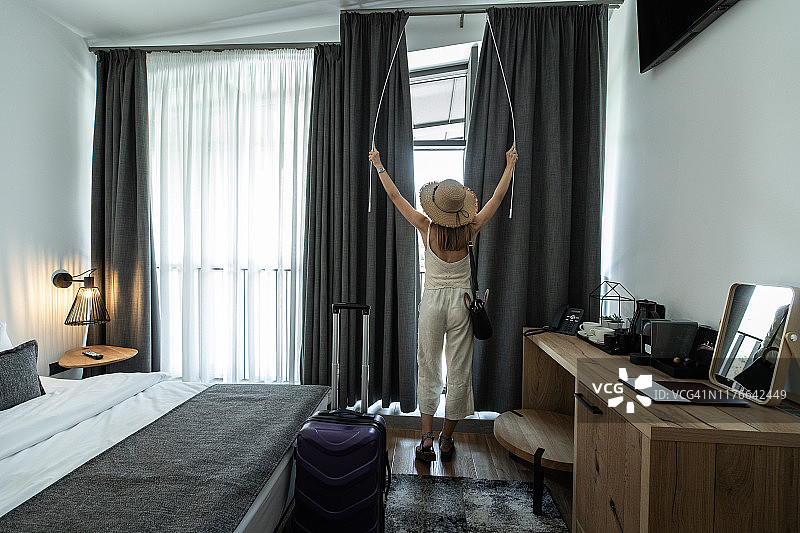 一个女人在酒店房间里拉开窗帘图片素材