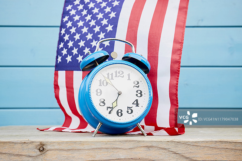 木制桌子上的复古闹钟，映衬着美国国旗和蓝色的木墙图片素材