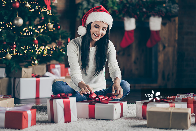 全尺寸照片的快乐积极的女孩坐在地板在她的房子与新年装饰花环为她的丈夫在圣诞夜派对庆祝戴圣诞老人帽室内准备梦想的礼物图片素材