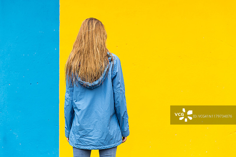 后视图的年轻女子与蓝色雨衣在彩色的背景图片素材