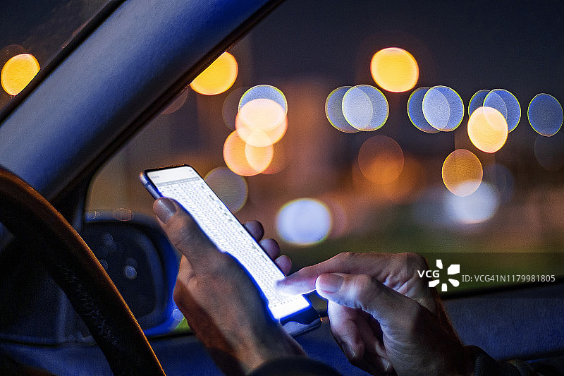 晚上在车里用智能手机的手的特写。图片素材