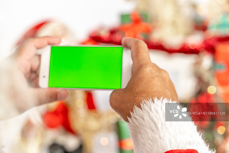 圣诞老人的手与智能手机与色度键绿色屏幕的特写图片素材