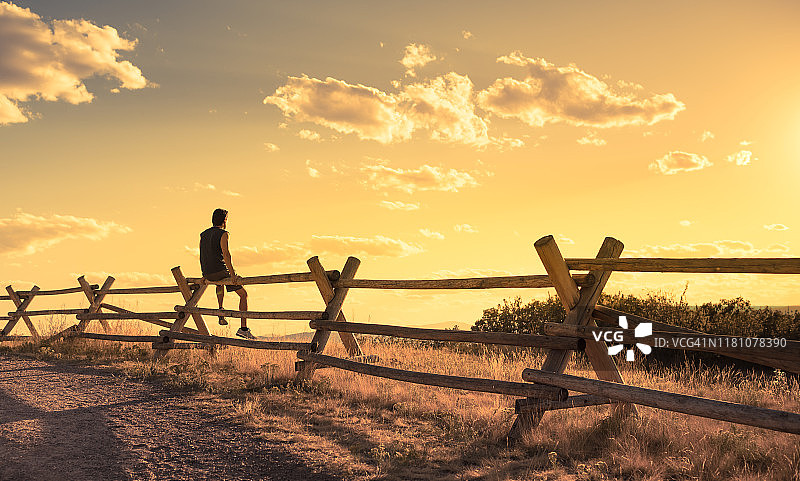 一个深思熟虑的年轻人坐在乡村里看美丽的日落。图片素材