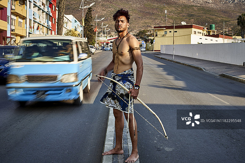 安哥拉的卢班戈，一个部落男子，在市中心带着他的传统拱门和箭，汽车经过图片素材