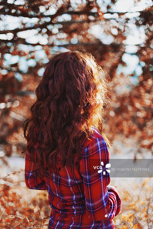 后视图的女人与长波浪红头发穿着长袖红色格子衬衫，大地色调图片素材