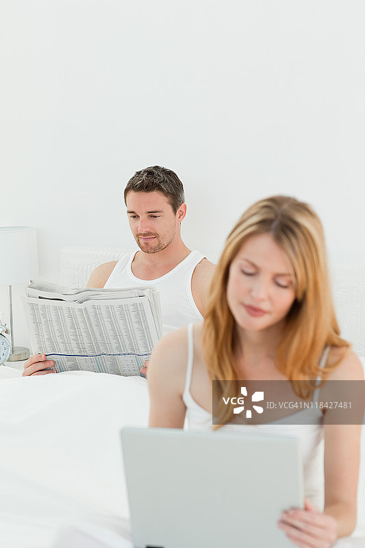 一个女人在看笔记本电脑，而她的丈夫正在看报纸图片素材